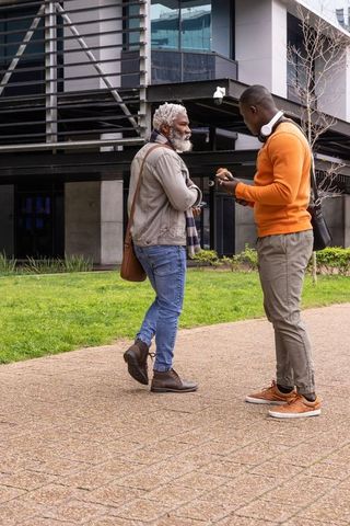 African american senior and adult sharing smartphone on urban sidewalk during casual talk