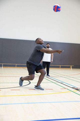 Athlete lunging and receiving volleyball while teammate observing on indoor court