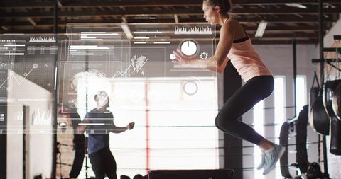Female athlete performing explosive plyo box jump in industrial gym with futuristic hud