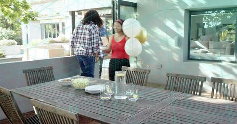 Sunlit outdoor dining table with lemon water pitcher and woman carrying balloons on patio