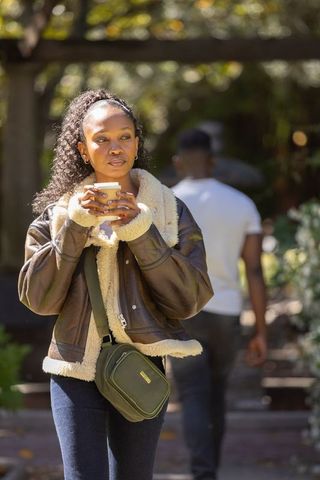 African american woman holding coffee walking sunlit garden wearing shearling jacket