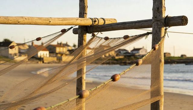 Sunlit fishing nets drying on wooden rack at coastal village beach with floating buoys
