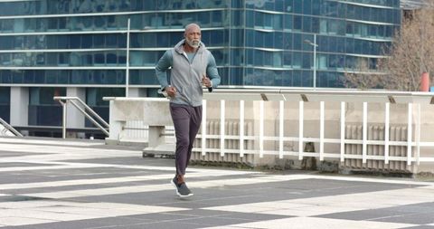 Senior African American man jogging across urban terrace by glass office building
