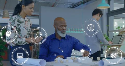 Diverse Coworkers Collaborating on Architectural Model with Digital Icons Overlay