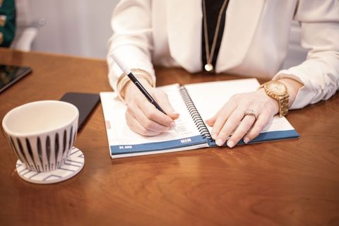 Woman writing notes in diary with coffee cup