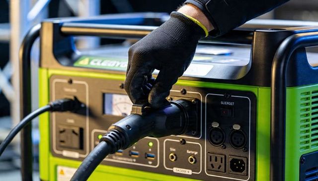 Gloved hand connecting locking plug to portable green power station with gauge and usb