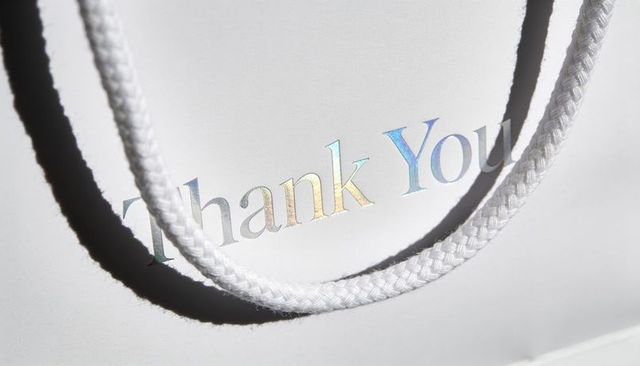 Minimalist white gift bag featuring holographic thank you foil and braided rope shadow
