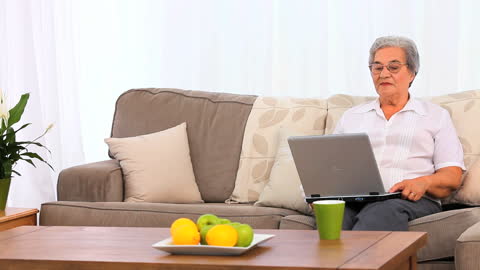 Elderly Woman Using Laptop While Relaxing on Comfortable Couch