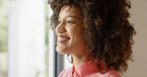 Young woman smiling while gazing out window in warm natural light closeup, curly hair