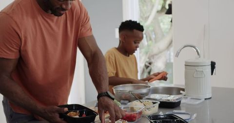 Father and teen son packing healthy meal-prep trays in bright home kitchen