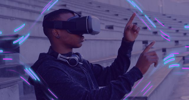Young man wearing VR headset engaging in an immersive digital experience outdoors, using hand gestures for interaction. Ideal for depicting modern technology, gaming, and virtual reality innovations. Perfect for use in tech blogs, websites, promotional material for VR products, and articles on the future of technology.