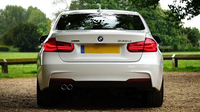 Luxury white BMW sedan seen from the rear in an outdoor setting with green trees and shrubs. Ideal for use in automobile reviews, car enthusiast blogs, marketing campaigns for BMW, and advertising for luxury car rental services.