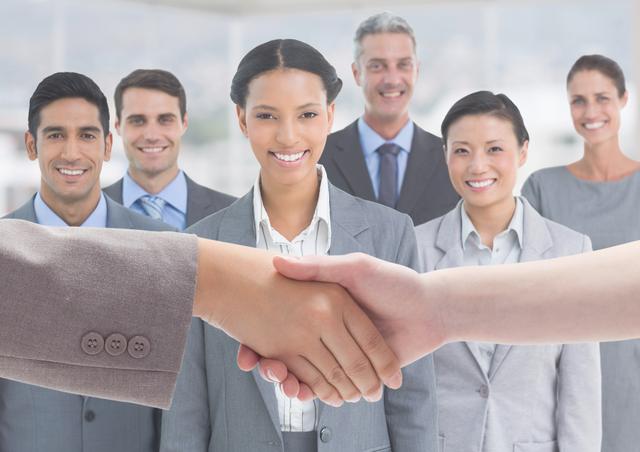 Hand of businesspeople shaking hands with smiling business executives in background