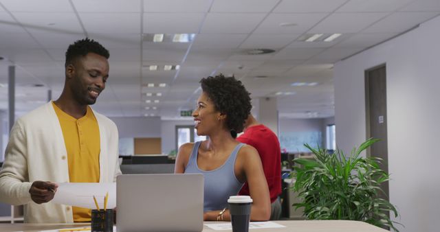 Happy african american male and female business colleagues talking and using laptop. working in business at a modern office.