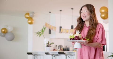Woman Holding Cake with Candles in Decorated Dining Room