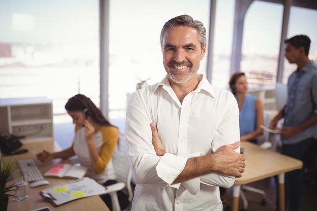 Portrait of smiling mature businessman with arms crossed standing in creative office