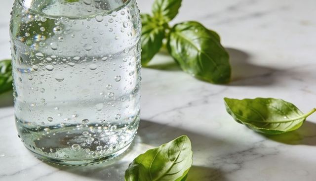 Sparkling mason jar with bubbles and fresh basil leaves on marble countertop