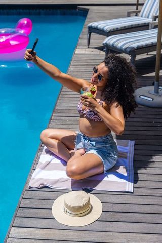 Poolside selfie by african american woman relaxing with cocktail at sunlit pool deck