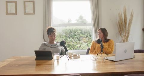 Multiracial women recording home podcast with laptop, tablet and tabletop microphones