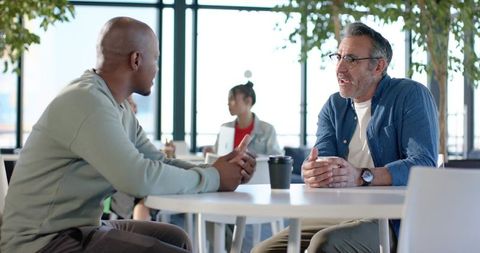 Diverse colleagues having candid conversation over coffee in modern coworking lounge