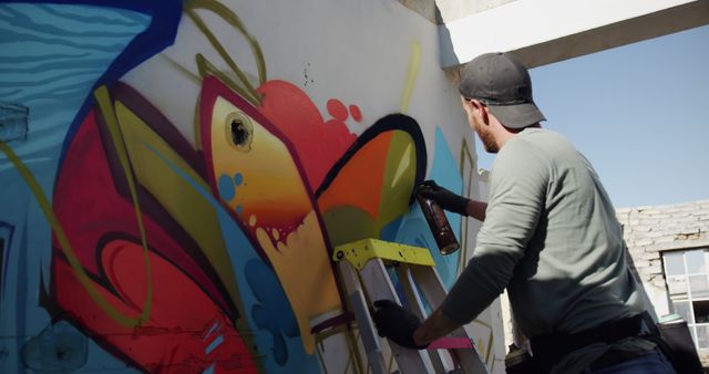 Caucasian male street artist graffitiing distressed wall. Street art, graffiti and urban lifestyle concept, unaltered.