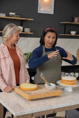 Diverse senior women teaching cake decorating and frosting techniques in modern kitchen