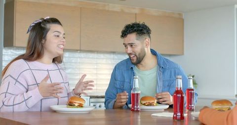 Friends sharing burgers and red soda at kitchen island laughing and chatting together
