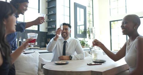 Sunlit friends toasting in modern kitchen celebrating team success with champagne