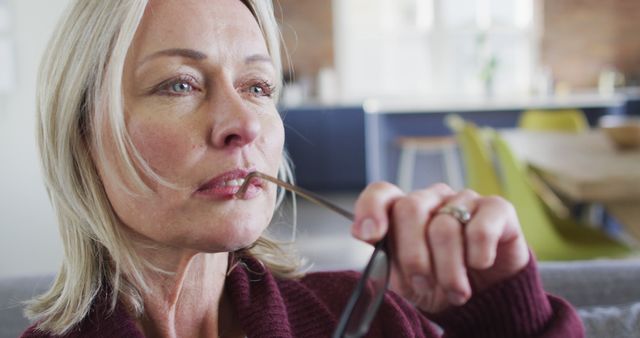 Thoughtful Mature Woman Pondering While Holding Glasses in Modern Kitchen - Download Free Stock Images Pikwizard.com