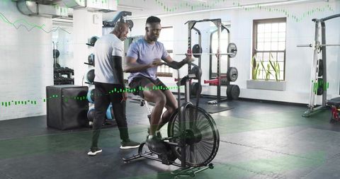 Trainer coaching man pedaling assault bike during high-intensity gym cardio session