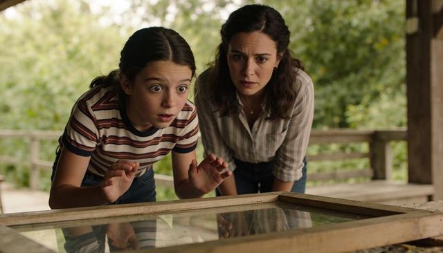 Mother and tween daughter discovering curiosity in framed glass on rustic porch