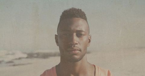African american man standing on sunny beach facing camera wearing orange tank, grainy vintage
