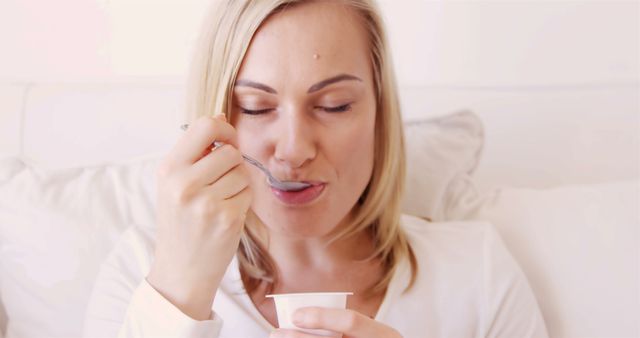 Blonde woman eating a yogurt at home