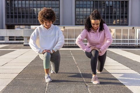 Diverse women stretching on urban rooftop wearing hoodies and leggings for morning workout