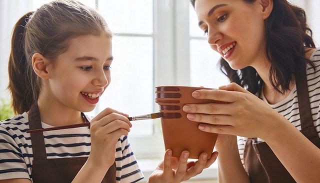 Mother teaching daughter painting terracotta pot together in sunlit kitchen