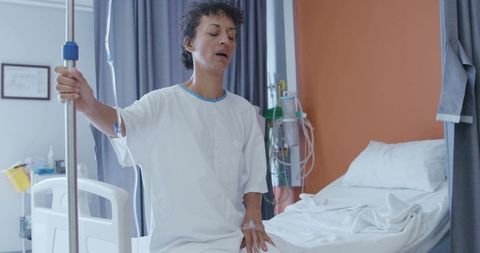 Patient holding iv pole while resting on hospital bed during recovery, medical treatment