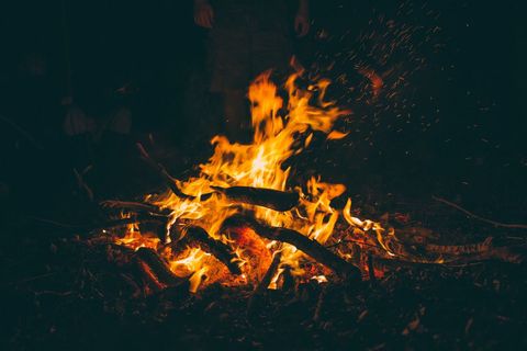 Campfire Flames and Glowing Embers at Night with Flying Sparks and Burning Logs