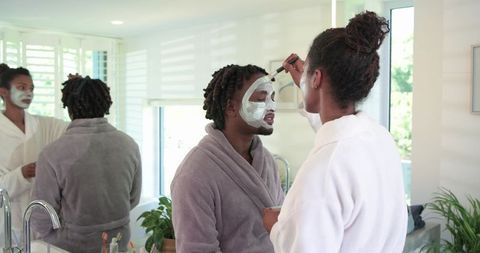 Couple applying facial mask at bathroom vanity wearing bathrobes, morning skincare ritual