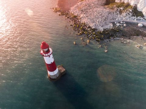 Aerial view of iconic lighthouse on rocky coastline at sunset