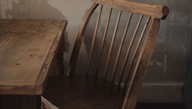 Rustic spindleback chair beside worn reclaimed wood table with peeling plaster wall