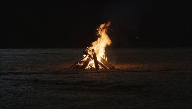 Bonfire burning on scorched ground at night with glowing flames and flying embers