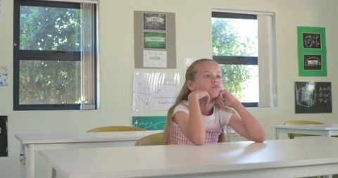 Preteen girl daydreaming at school desk resting chin on hands sunlit classroom calm
