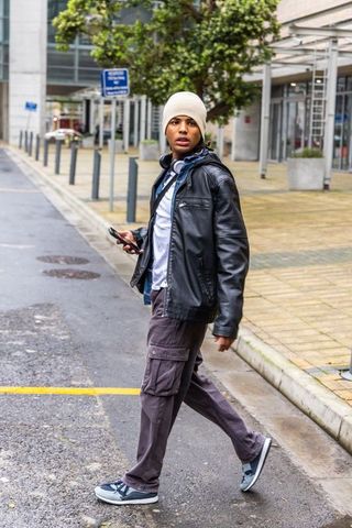 African american man crossing wet urban plaza holding smartphone wearing beanie headphones