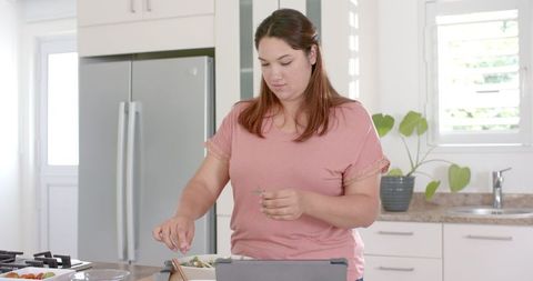 Young Woman Prepping Salad in Modern Kitchen with Tablet