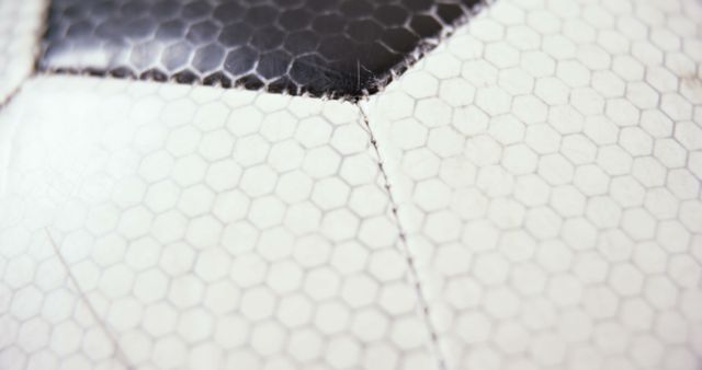 Detailed close-up of a worn soccer ball showcasing the hexagonal patterns and stitching. This image can be used for sports-related themes, emphasizing wear and tear, durability of sports equipment, or adding texture and close-up interest to athletic or nostalgic designs.