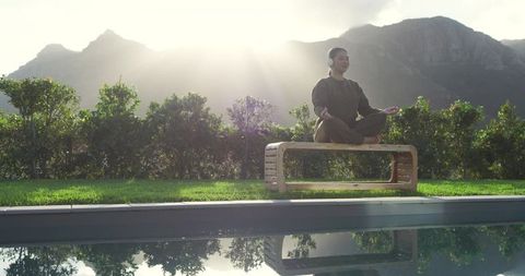 Woman Meditating by Pool Surrounded by Mountains at Sunrise