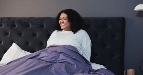 Middle-aged African American woman smiling in bed with tufted headboard and gray decor