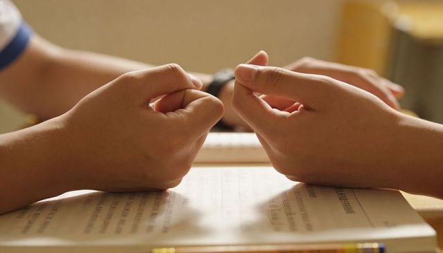 Students counting fingers over open textbook on wooden desk with pencil and wristwatch