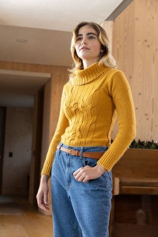Woman in mustard sweater standing in rustic interior with piano