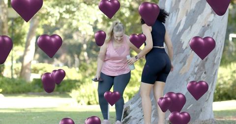Two women exercising and checking phone at park beside tree with purple heart overlays